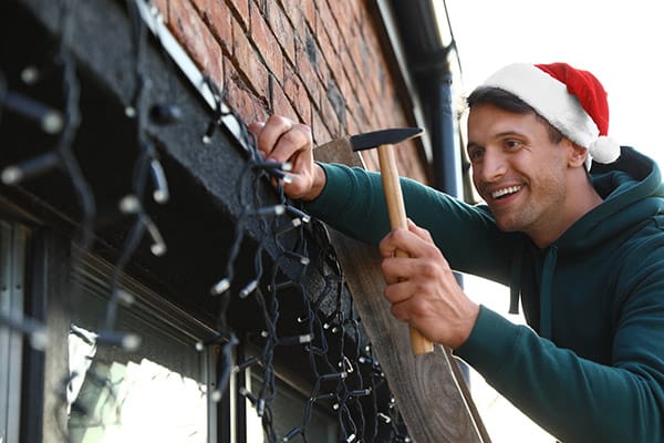 man installing Christmas lights around windows outdoors