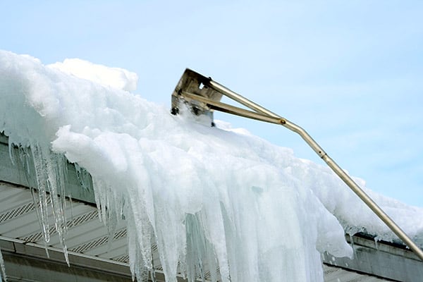 someone-removing-snow-from-a-roof-using-a-snow-rake