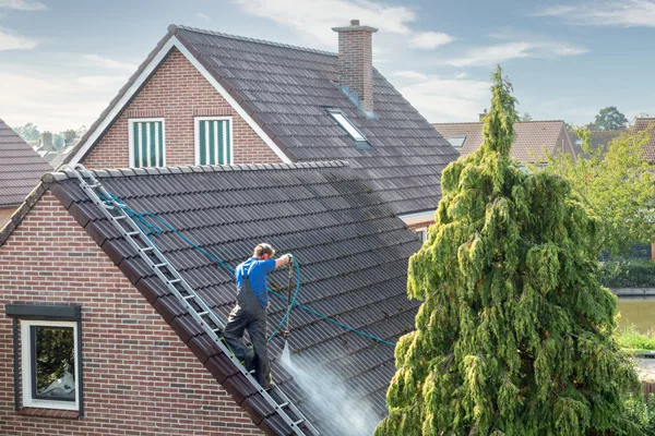 a man cleaning asphalt shingles with a hose